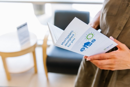 Photo of a person holding a Servus brochure named "Mortgages designed for you" in a Servus branch.